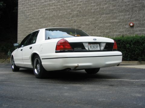 1998 Ford Crown Victoria - This white 1998 Ford Crown Victoria is parked outside a brick building.
