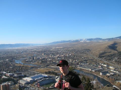 1996 Ford Bronco - A young man wearing a black baseball cap and backpack stands on a hill overlooking a city and distant mountains.