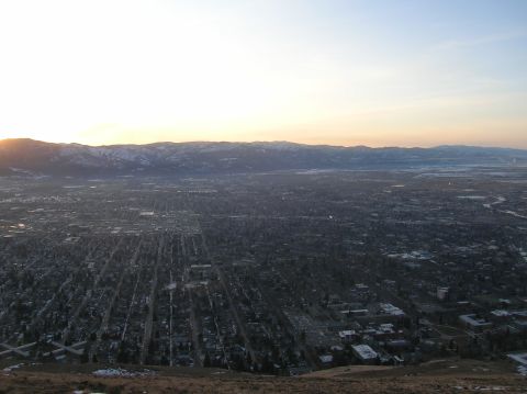 1996 Ford Bronco - A wide aerial view of a city nestled in a valley at sunset, with snow-capped mountains in the distance.