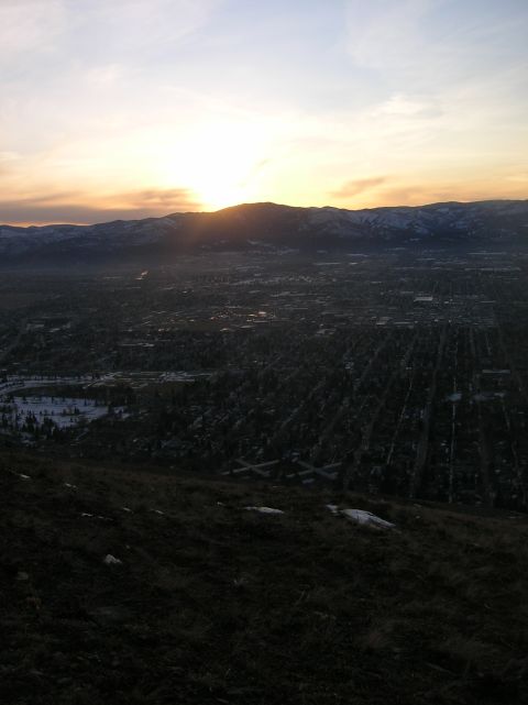 1996 Ford Bronco - A panoramic view of a city nestled in a valley at sunset, with mountains in the background. The foreground shows a grassy slope.