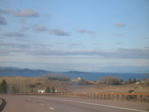 1996 Ford Bronco - A scenic view of a body of water with distant mountains under a cloudy sky. A highway curves through the foreground with a wooden guardrail.