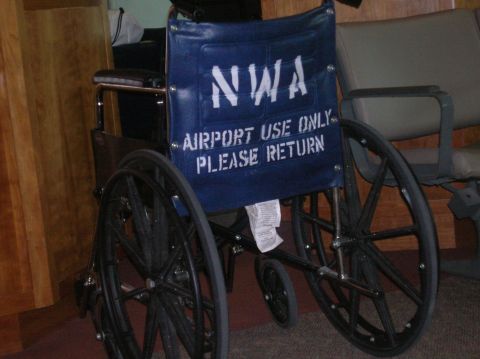 1996 Ford Bronco - A blue wheelchair with white lettering that reads "NWA AIRPORT USE ONLY PLEASE RETURN" is shown in a room with wooden paneling and chairs i…