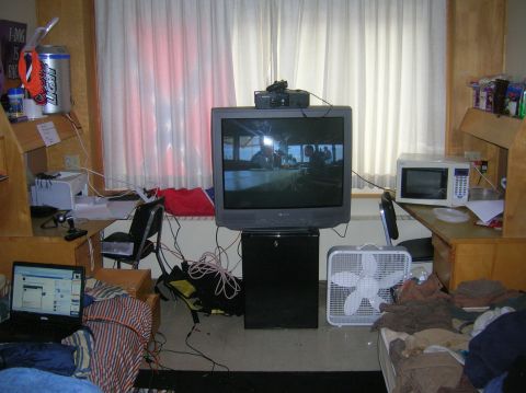 1996 Ford Bronco - A cluttered dorm room scene with a television, microwave, fan, and a laptop on a bed.
