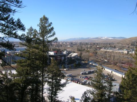 1996 Ford Bronco - A panoramic view of a city nestled in a valley with mountains in the distance. In the foreground, evergreen trees partially obscure a stadi…