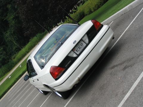 1998 Ford Crown Victoria - The rear of a white sedan is shown parked in a lot with trees in the background.