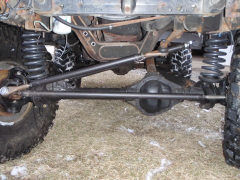 1996 Ford Bronco - The underside of a 1996 Ford Bronco shows the front axle, suspension components, and steering linkage. The vehicle is parked on a grassy ar…