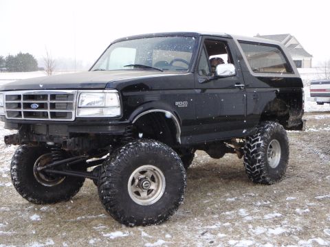 1996 Ford Bronco - A lifted black 1996 Ford Bronco with large off-road tires sits in a snowy, grassy field. The front of the vehicle shows a chrome grille and…