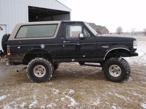 1996 Ford Bronco - A lifted black 1996 Ford Bronco with a tan top is parked on a grassy area with patches of snow. The vehicle has large off-road tires and a…