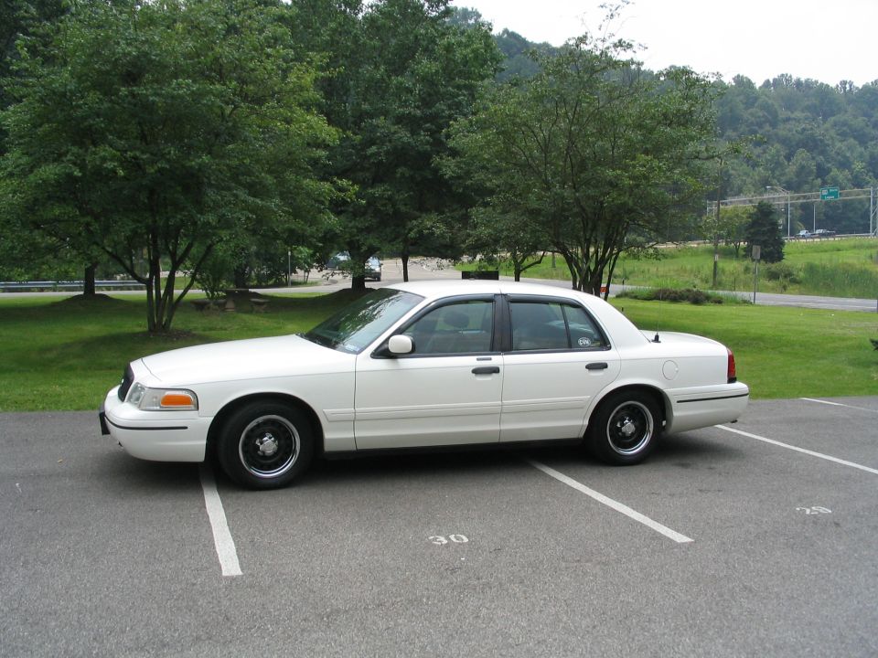 White Ford Crown Victoria sedan side profile on black steel wheels in a parking lot