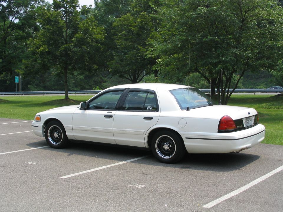 White Ford Crown Victoria sedan with black steel wheels, 3/4 rear view in parking lot