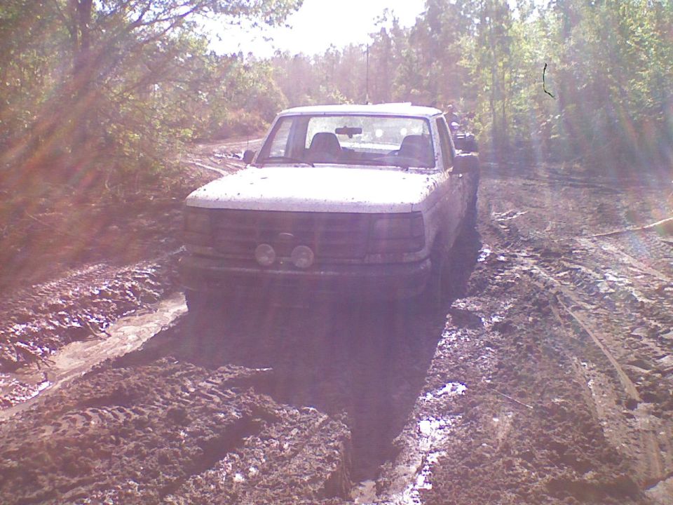 White Ford truck crossing a deep muddy section of trail