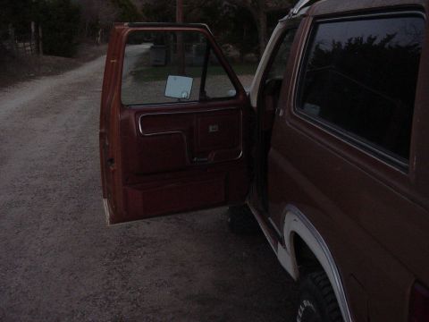 1982 Ford Bronco - The driver's side door of a brown Bronco is open, revealing the interior door panel and a glimpse of the exterior.