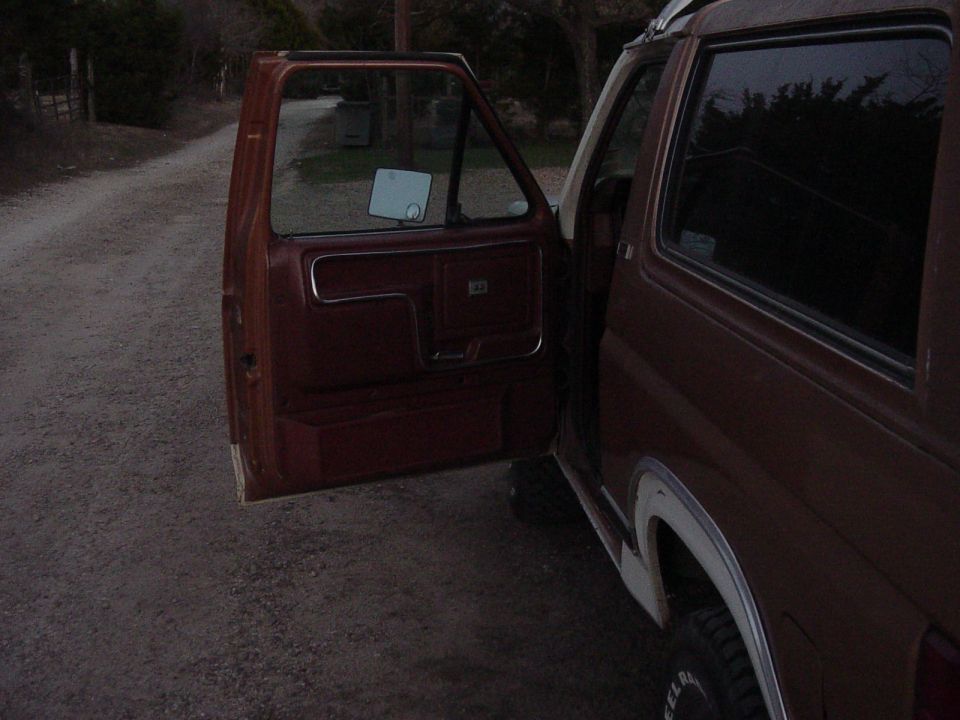 Side view of a brown Ford Bronco with the driver's door open, showing the interior panel