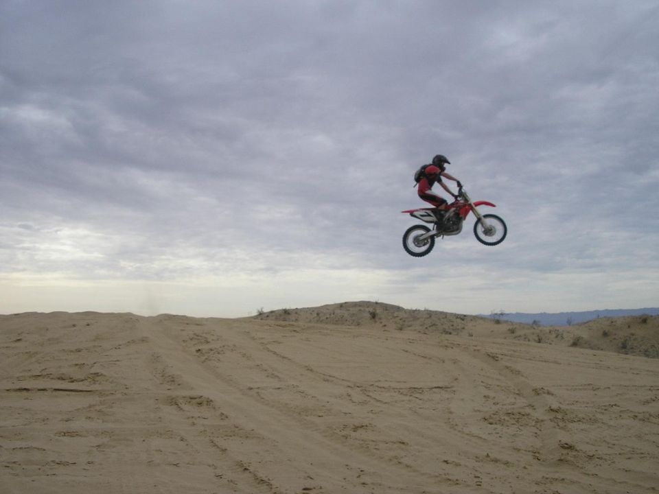 Red dirt bike jumping in the air over sand dunes