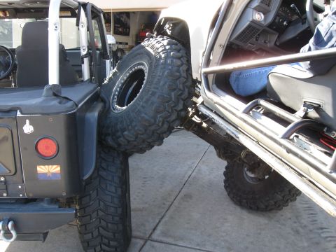 2004 Jeep Wrangler - A black Jeep Wrangler is parked next to a white Jeep Wrangler, with the tires of both vehicles making contact. The black Jeep has a spare t…
