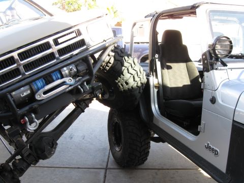 2004 Jeep Wrangler - A silver Jeep Wrangler is parked next to a modified truck with a winch and off-road tires. The Jeep's driver's side door is open, revealing…