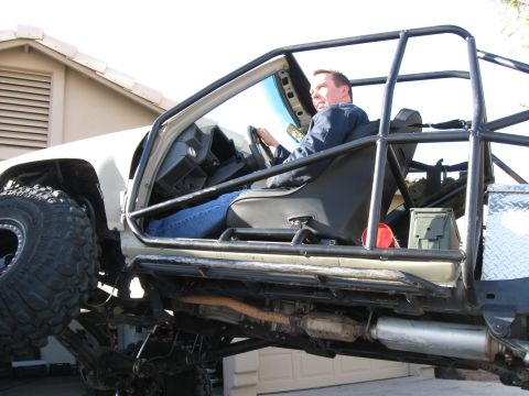 2004 Jeep Wrangler - A man sits in the driver's seat of a heavily modified off-road vehicle with a prominent roll cage. The vehicle has large tires and appears…