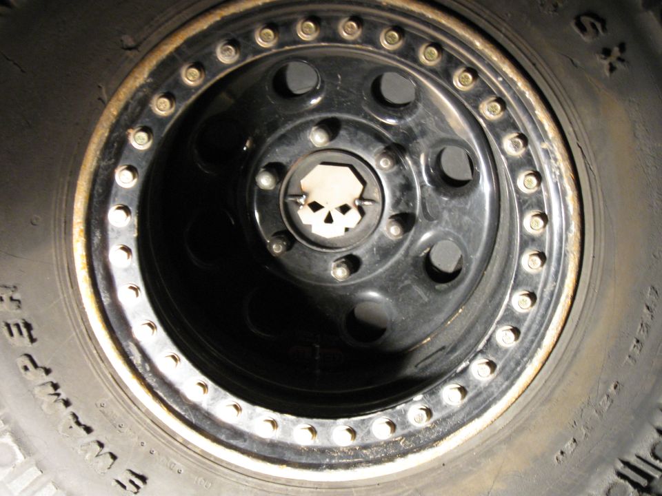 Black aftermarket wheel with skull center cap on Jeep Wrangler tire.