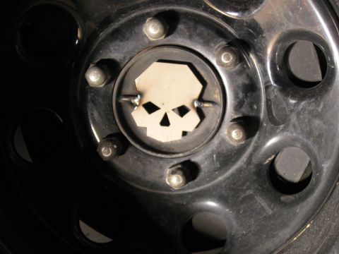 2004 Jeep Wrangler - A close-up view of a black wheel hub with a custom skull-shaped metal insert. The insert is secured with two small welds.