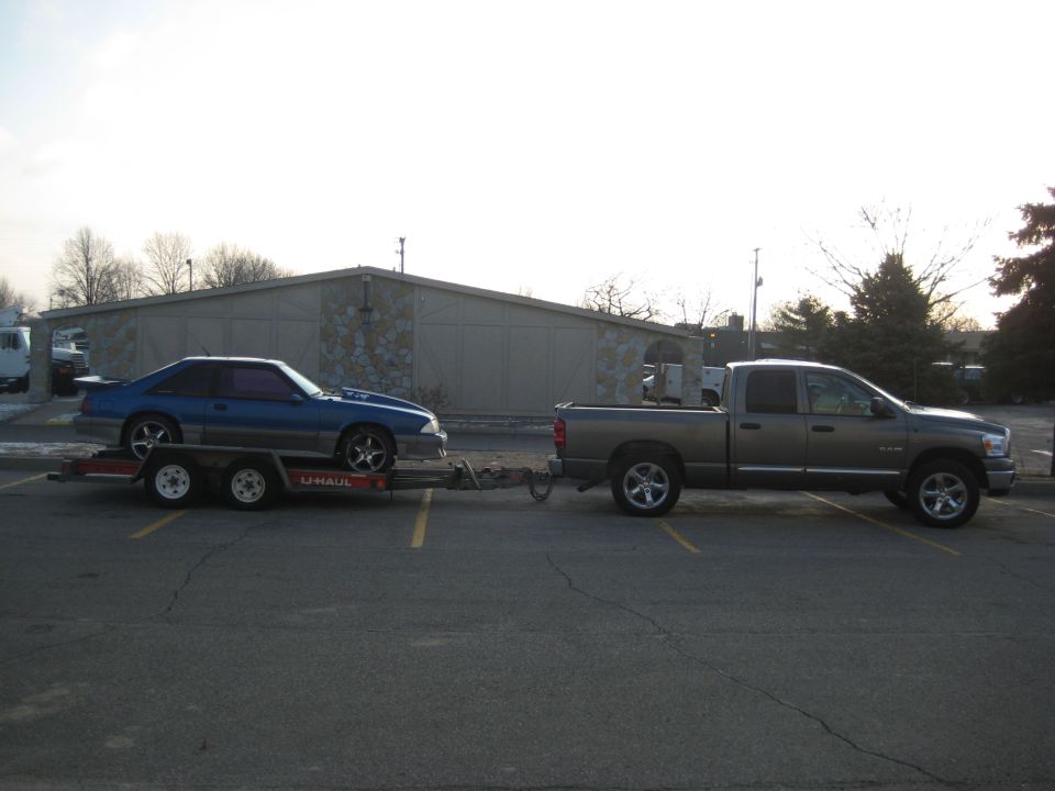 Blue Ford Mustang on a U-Haul trailer towed by a gray Dodge Ram pickup truck.