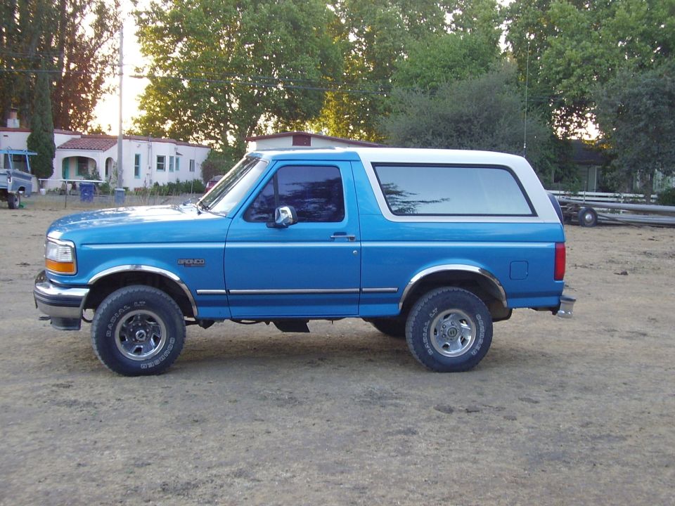 Blue Ford Bronco with white top parked on dry grass, side view