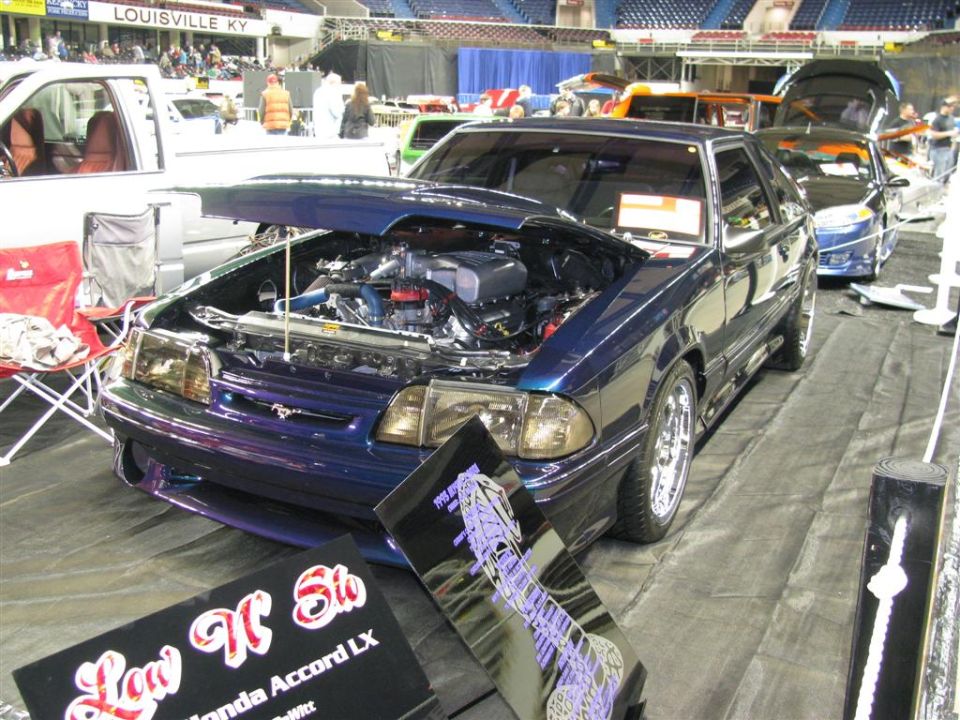 Dark blue custom Ford Mustang with hood open, showing engine, parked indoors.