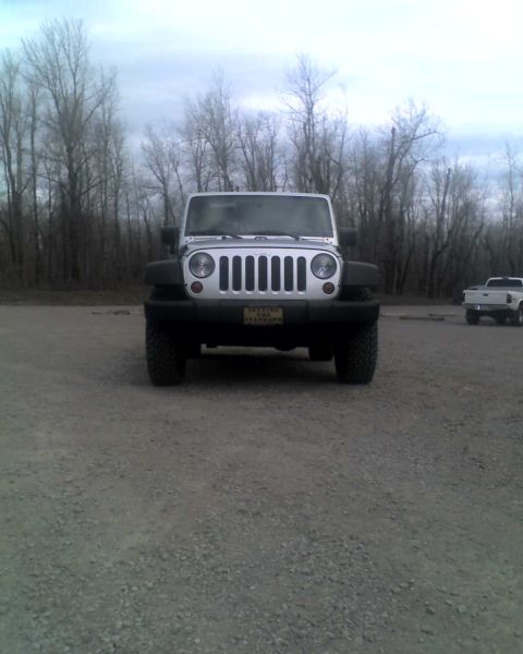 2005 Jeep Wrangler - A silver Jeep Wrangler is parked on a gravel lot with a line of bare trees in the background. The Jeep has a license plate that reads "SETT…