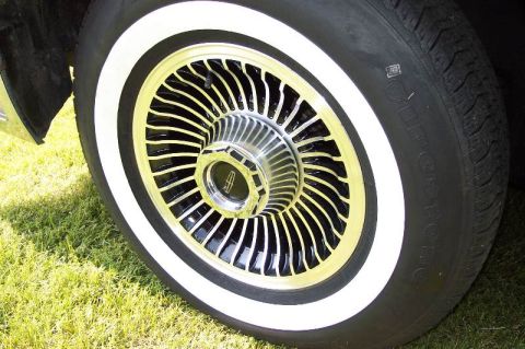 1988 Mercury Grand Marquis - A close-up view of a whitewall tire and a chrome and black wire wheel with a Lincoln logo on the hubcap. The vehicle is parked on a grassy…