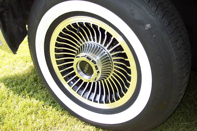Close-up of a whitewall tire and a chrome and black wire wheel with a Lincoln logo.