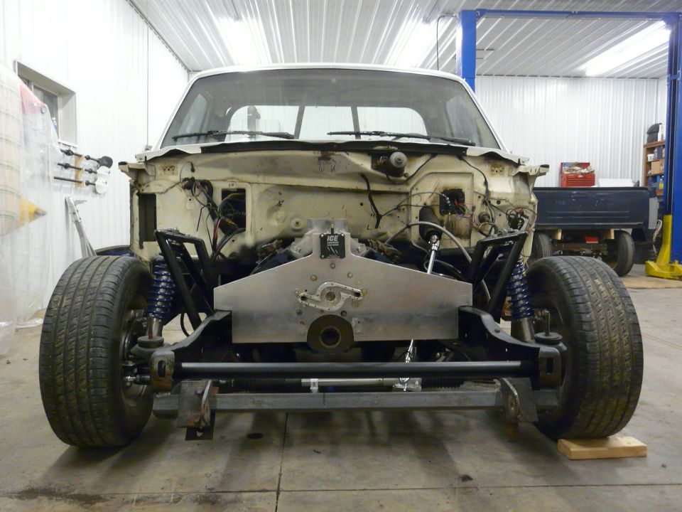 Stripped Ford pickup front end with tubular A-arm suspension and blue coilovers in a shop