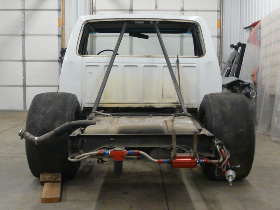 White pickup cab and frame with bed removed showing cage bars, fuel tank and AN plumbing