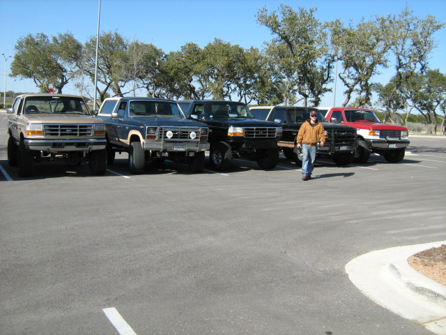 Row of five lifted full-size Ford Broncos parked in a lot with a man walking in front