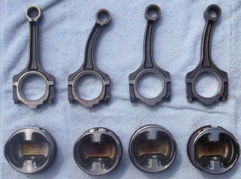 1997 Ford Taurus - Four connecting rods and four pistons are laid out on a blue towel. The connecting rods are arranged in two rows of two, with the pistons b…