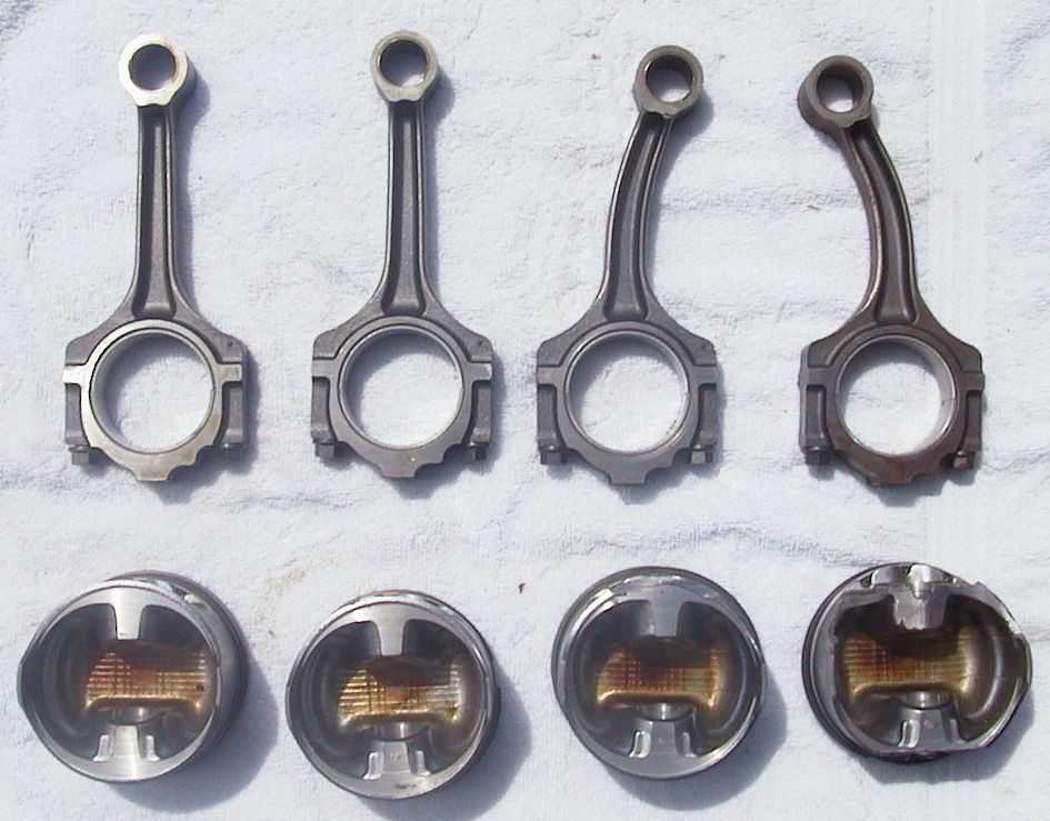 Four connecting rods and four pistons laid out on a white surface.