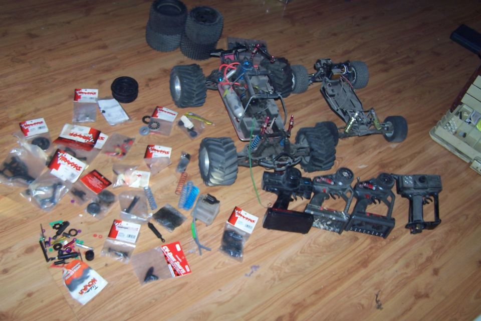 Two remote control cars, several controllers, and a pile of parts laid out on a wooden floor