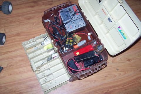 2004 Arctic Cat F-7 Firecat - An open tackle box contains RC car batteries, a charger, and various small parts, with a partial view of two RC car tires on the left.