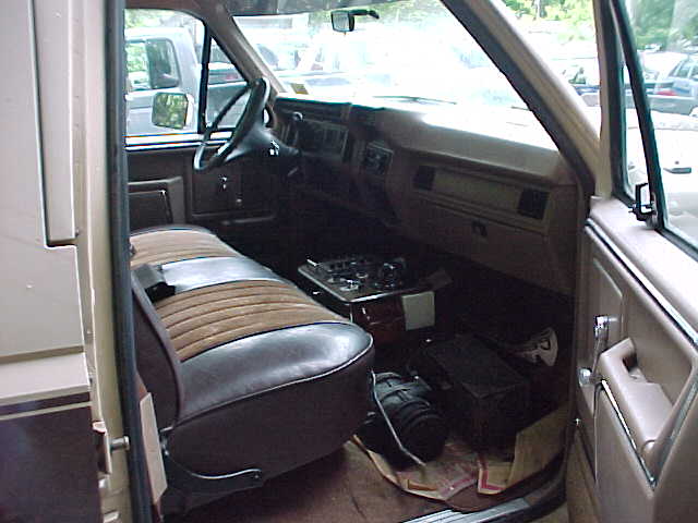 Interior of Ford truck through passenger door showing brown/tan bench seat, tan dash, and gear on floor