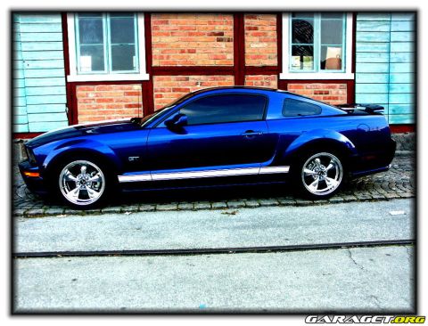 1998 Ford Crown Victoria - Side view of a blue 2005 Ford Mustang GT parked on a cobblestone street.