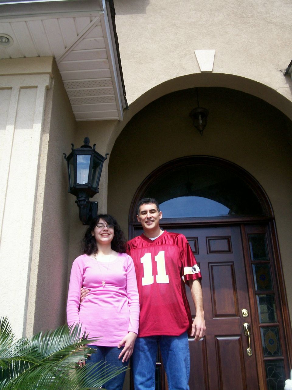 Couple in front of a dark wood door with arched window above. Man wears a red jersey with number 11