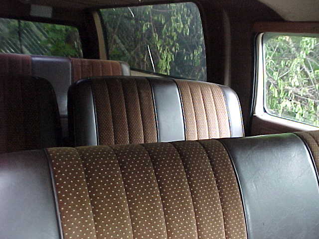 Brown and tan cloth bench seats inside a truck interior with windows showing green foliage