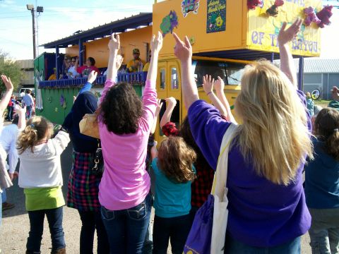 1993 Ford Bronco - A festive Mardi Gras parade float, decorated in yellow and purple, moves down the street as onlookers wave.