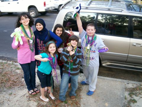 1993 Ford Bronco - Children and teenagers pose for a photo during Mardi Gras celebrations, with vehicles in the background.