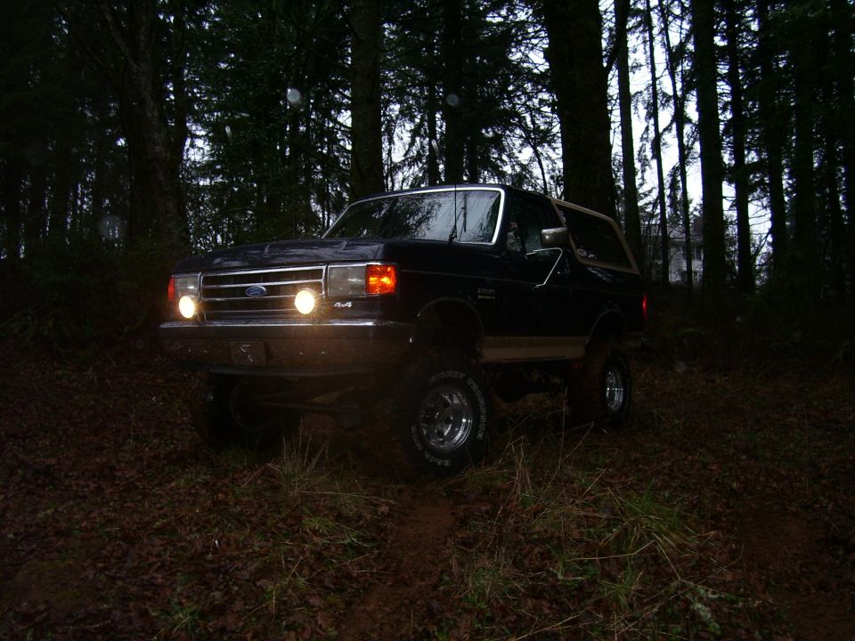 Ford Bronco driving on a dirt path in a forest at dusk. It has 4x4 badging
