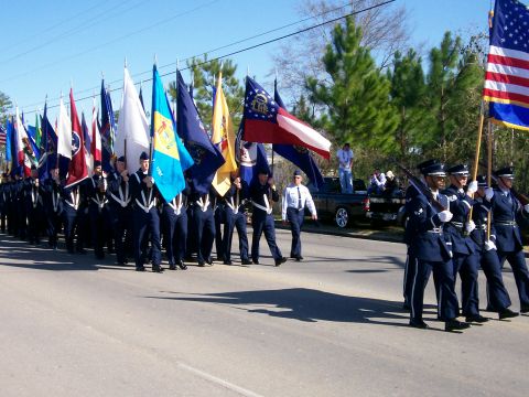 1993 Ford Bronco - A parade is underway with participants carrying various flags and marching in uniform, while a pickup truck is visible in the background.