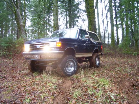 1991 Ford Bronco - This 1991 Ford Bronco is shown off-roading through a forest with its headlights on.