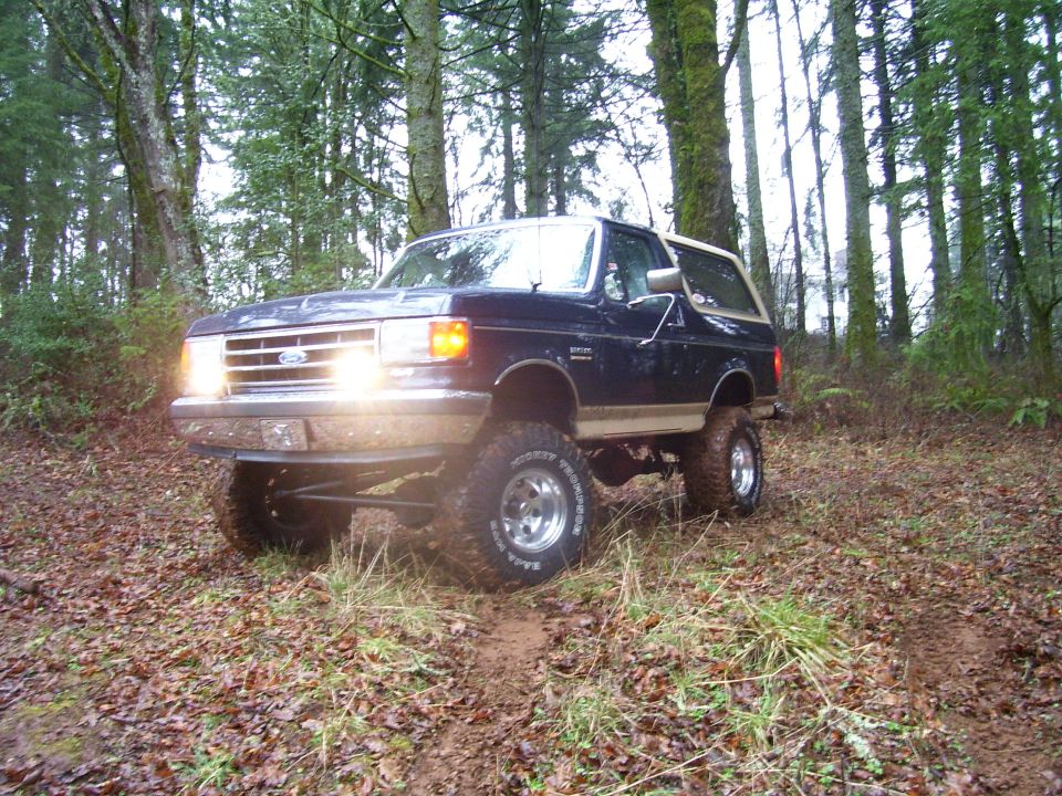 1991 Ford Bronco with lifted suspension driving on a dirt path in a wooded area