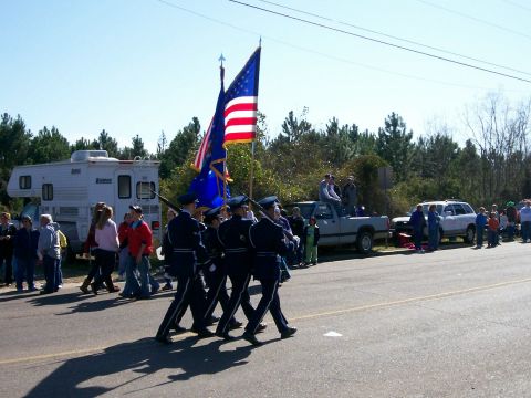 1993 Ford Bronco - A color guard marches down a street during a parade, with spectators lining the road and several vehicles present.