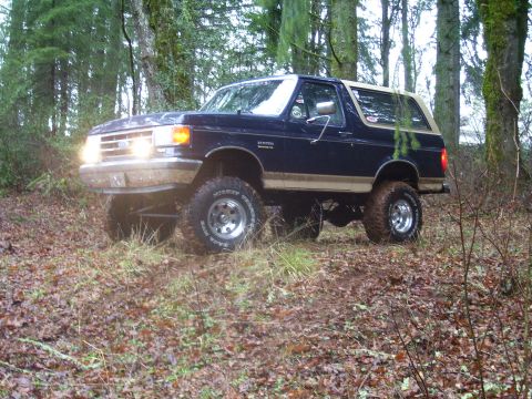 1991 Ford Bronco - A lifted Ford Bronco navigates a muddy forest trail.