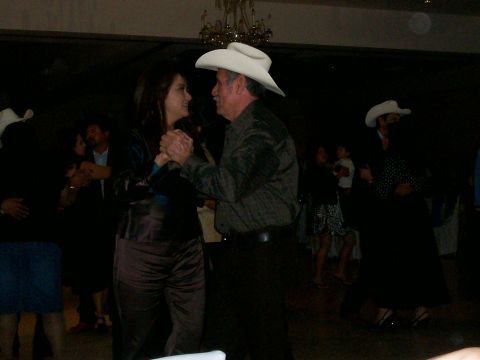 1993 Ford Bronco - Dimly lit indoor dance floor where a couple dances in the foreground, one wearing a white cowboy hat, with other guests and a chandelier be…