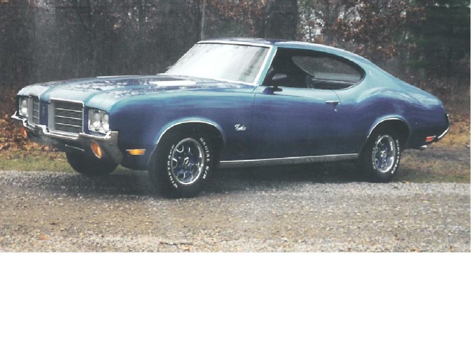 Blue coupe with chrome grille and trim, parked on gravel